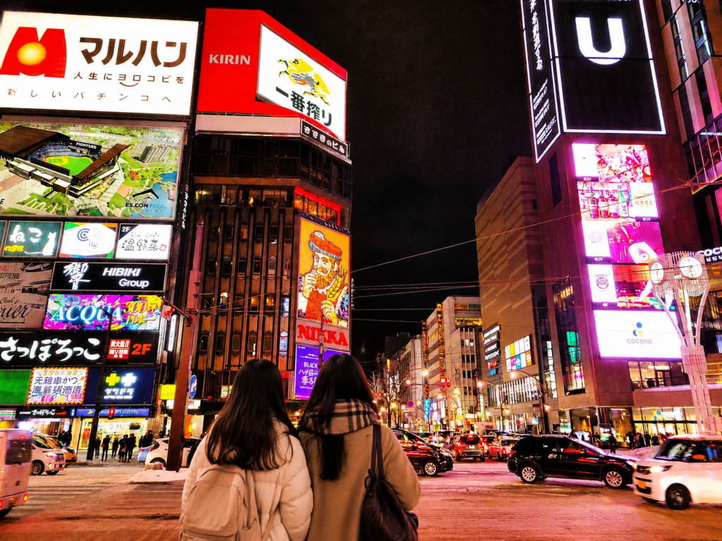 札幌すすきのの夜景を眺める旅行者の後ろ姿とネオン街のイメージ